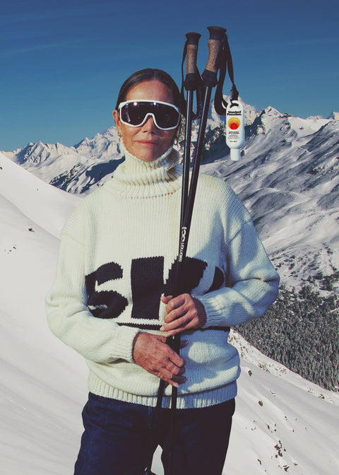 Person in ski gear with skis and poles against a snowy mountain backdrop
