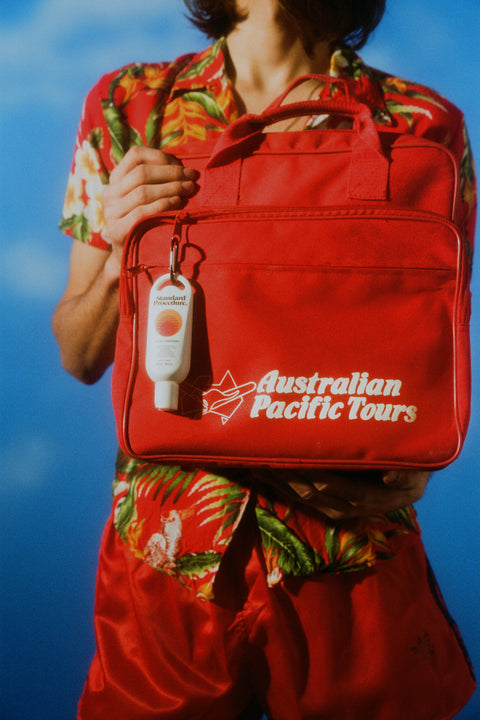Best sunscreen lotion SPF 50 clipped to a red Australian Pacific Tours bag held by a person in tropical attire.