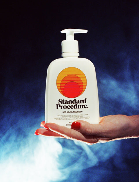 SPF 50 sunscreen pump bottle held in a hand against a smoky blue backdrop.