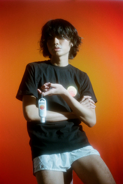 Sunscreen cream SPF 50 in a travel-size bottle held by a person wearing a black shirt against an orange gradient background.