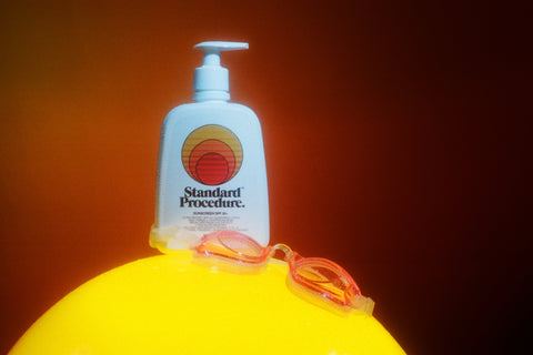 Sunblock lotion SPF 50 bottle placed on a bright yellow surface with swimming goggles against a warm orange background.
