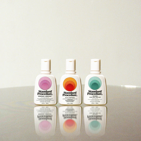 Sunscreen lotion SPF 50 bottle from Standard Procedure displayed with personal care products on a reflective surface.