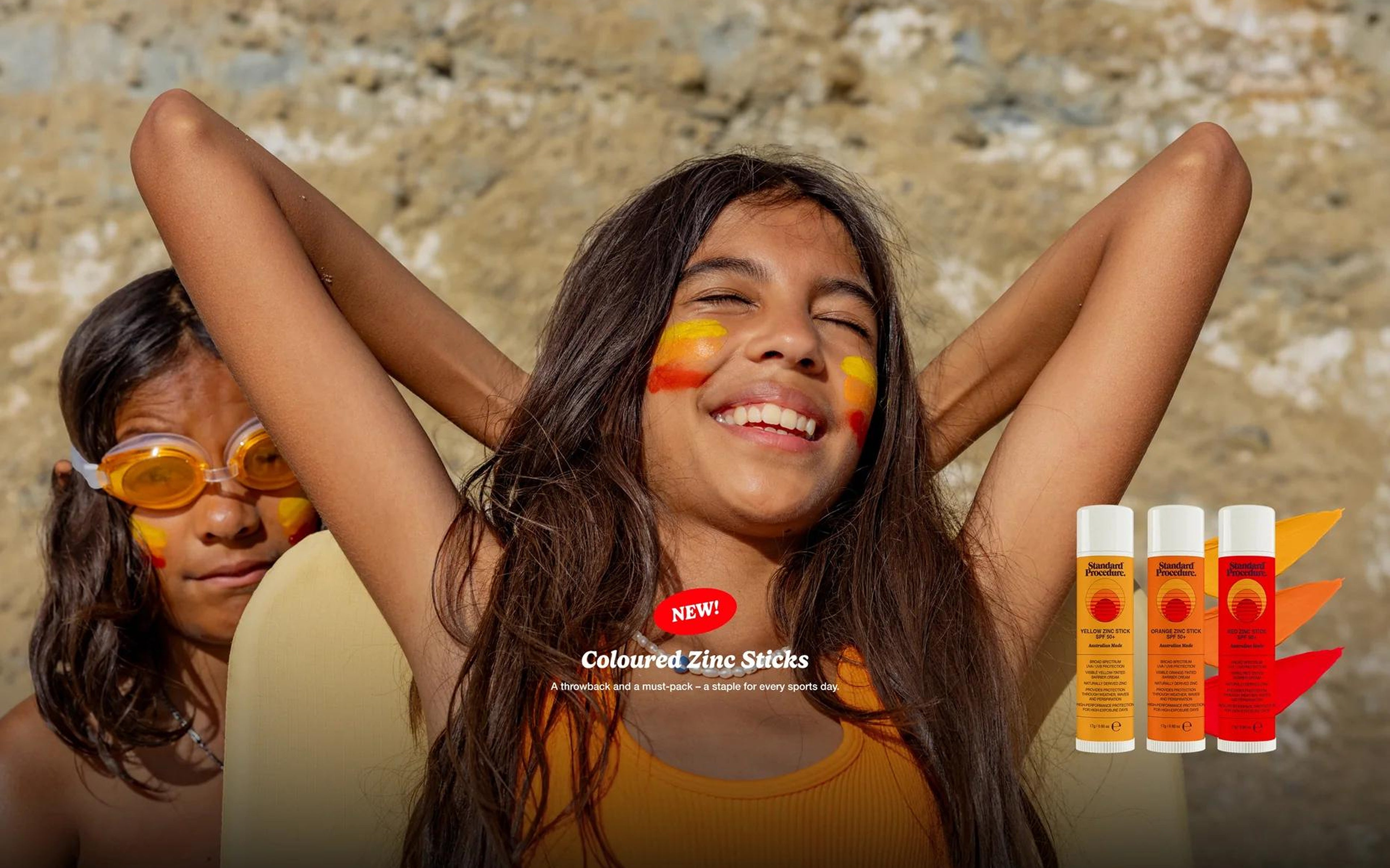 Child with coloured zinc stripes on the beach beside Standard Procedure zinc sticks and SPF 50+ sunscreen.