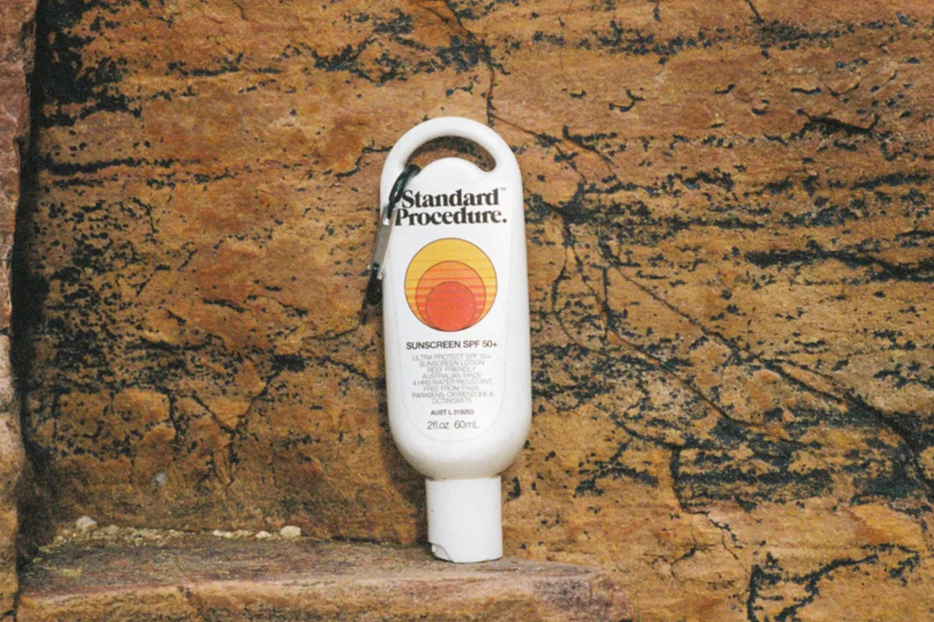 Australian sunscreen bottle of Standard Procedure SPF 50+ displayed against a rugged, textured rock background.