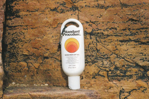 Australian sunscreen bottle of Standard Procedure SPF 50+ displayed against a rugged, textured rock background.