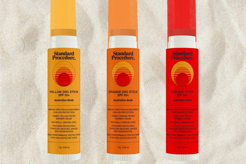 Standard Procedure daily SPF use zinc sticks in yellow orange and red displayed on sand