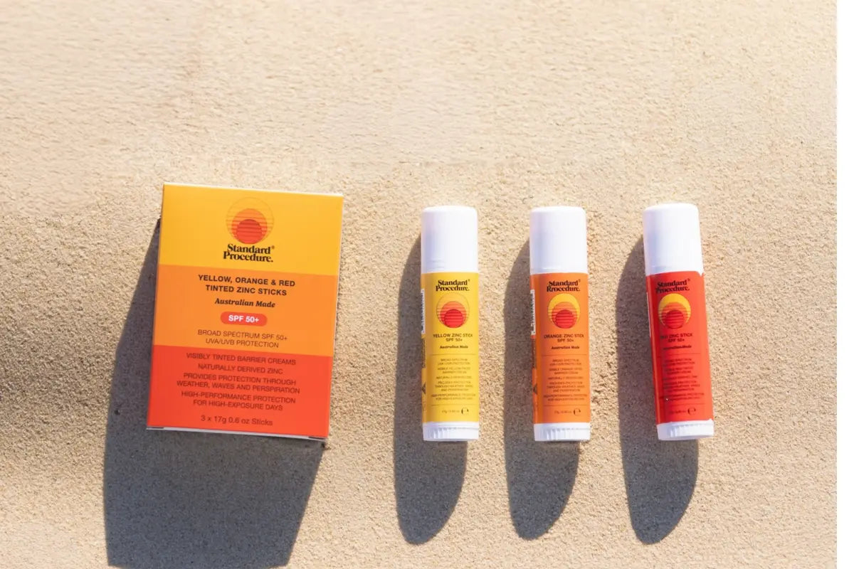 Standard Procedure tinted zinc sticks for daily use of sunscreen laid out on sand