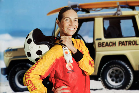 High SPF sunscreen carried by a smiling beach lifeguard standing in front of a rescue vehicle on the sand