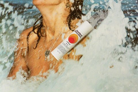 Lip balm with SPF tube displayed against a background of ocean waves splashing around a person in the water