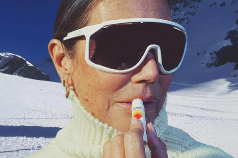 SPF lip balm being applied by a woman in ski gear on a snowy mountain