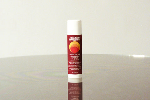 Lip balm with sunscreen SPF 50+ standing upright on a reflective surface against a neutral background