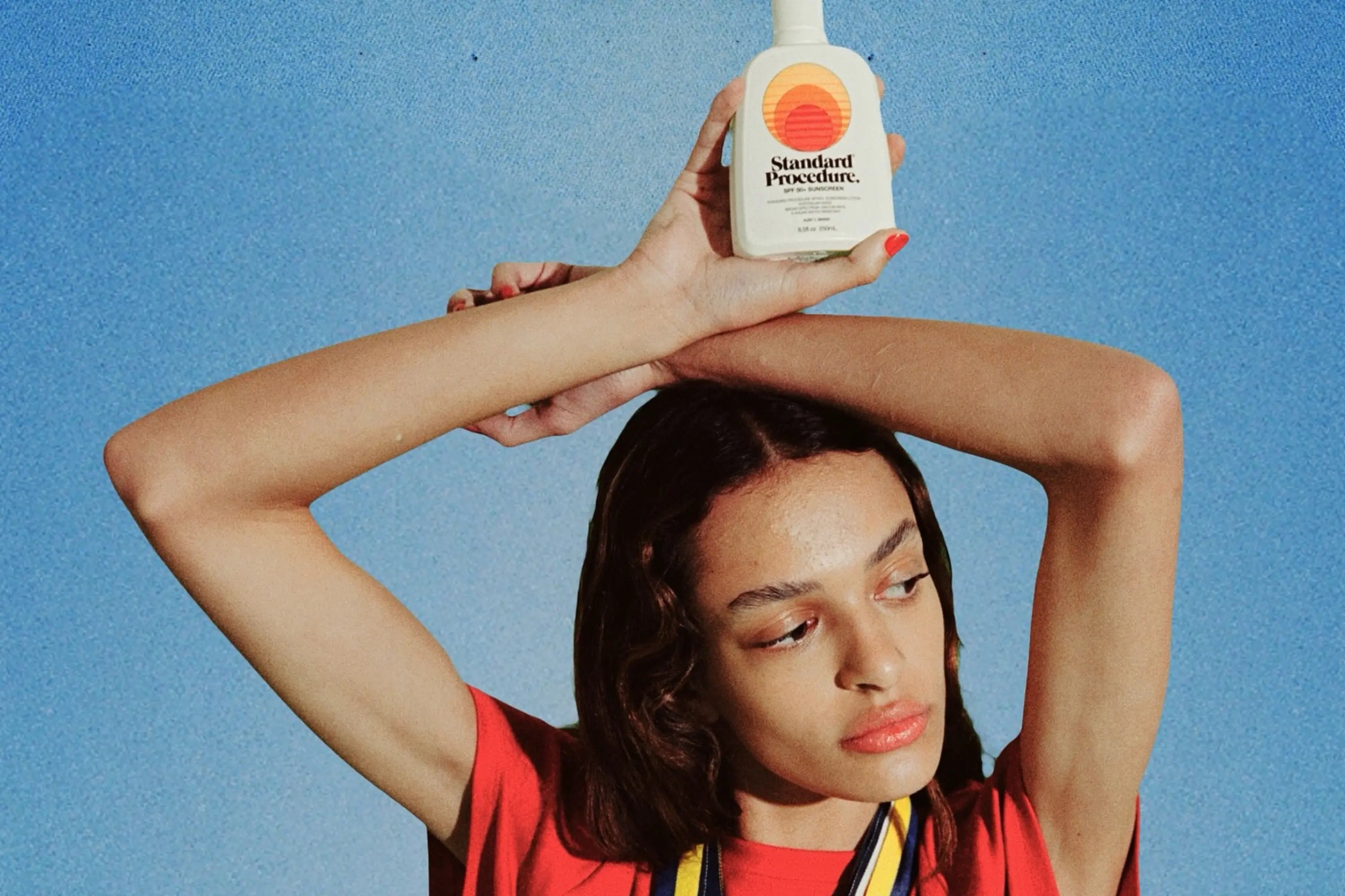 Non-toxic sunscreen held above a model's head against a bold blue background
