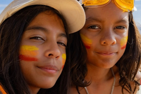 Safe SPF for children applied in colorful stripes on two smiling kids' cheeks at the beach