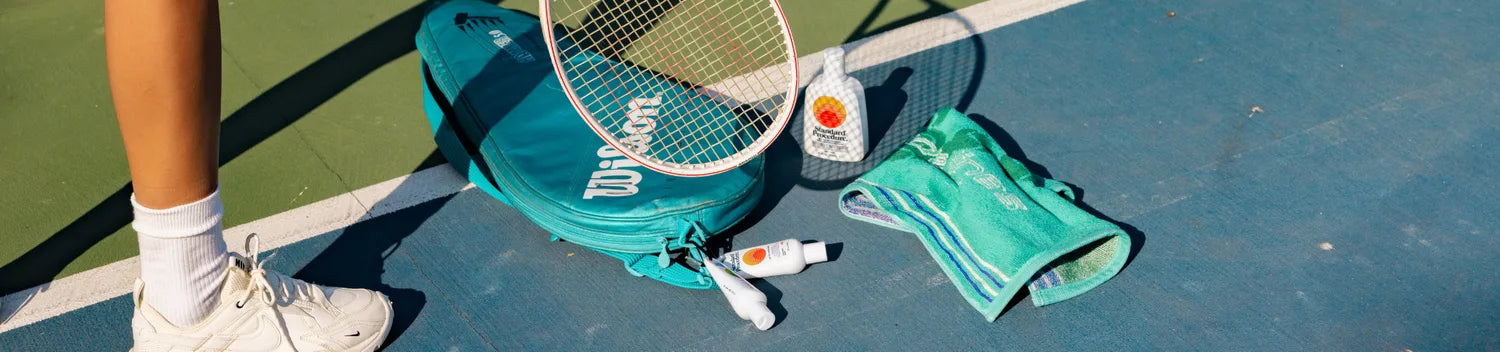Standard Procedure sunscreen bundle laid out on a sunny tennis court with bag and racket.