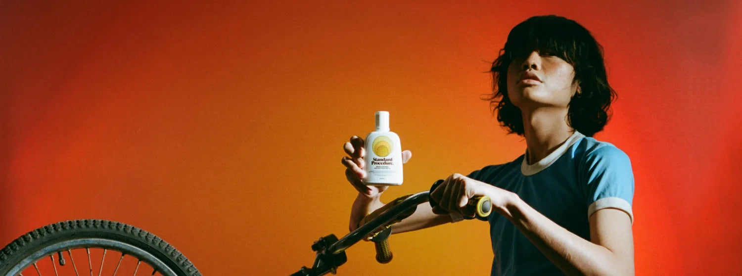 Person on a bike holding a Standard Procedure broad spectrum SPF 15 moisturiser bottle.