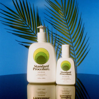 Aloe vera sun gel bottles from Standard Procedure displayed with tropical palm shadows and a reflective surface, emphasizing soothing, cooling after-sun skincare made with natural aloe