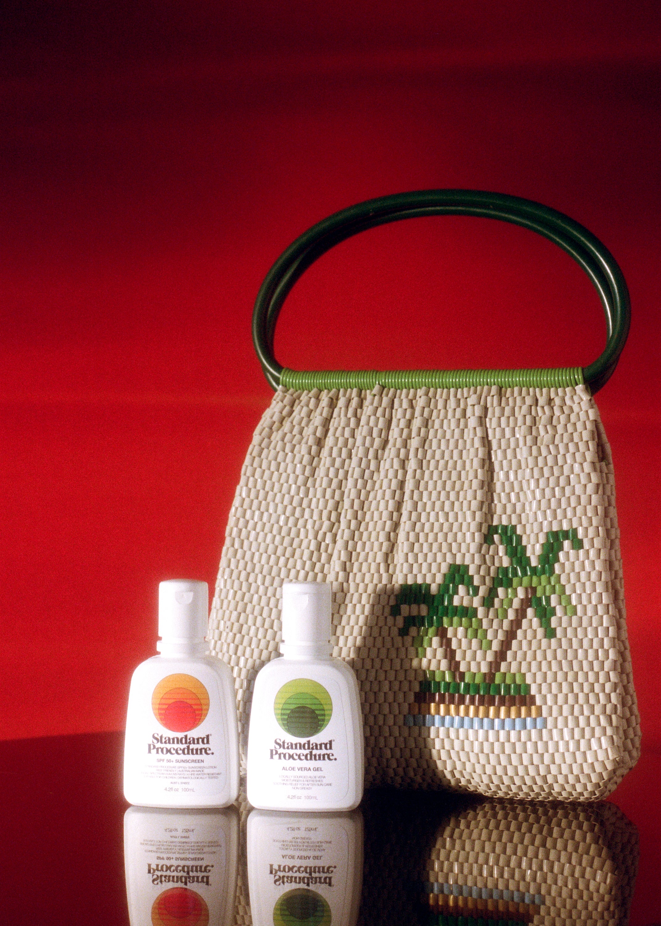 Aloe vera for skin and SPF 50+ sunscreen bottles from Standard Procedure placed beside a woven tropical handbag, highlighting natural hydration and sun protection essentials for after-sun care
