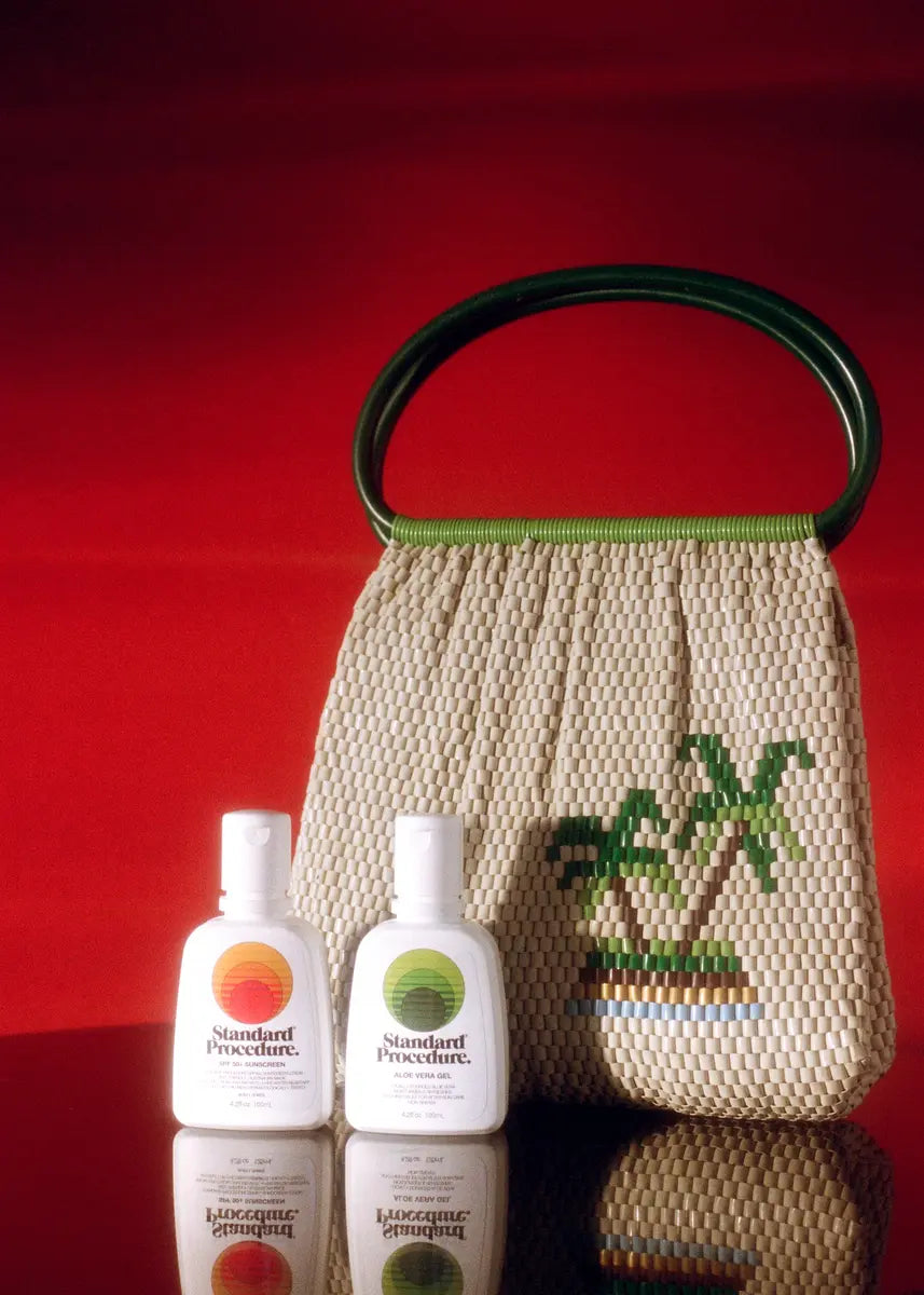 Aloe vera for skin and SPF 50+ sunscreen bottles from Standard Procedure placed beside a woven tropical handbag, highlighting natural hydration and sun protection essentials for after-sun care