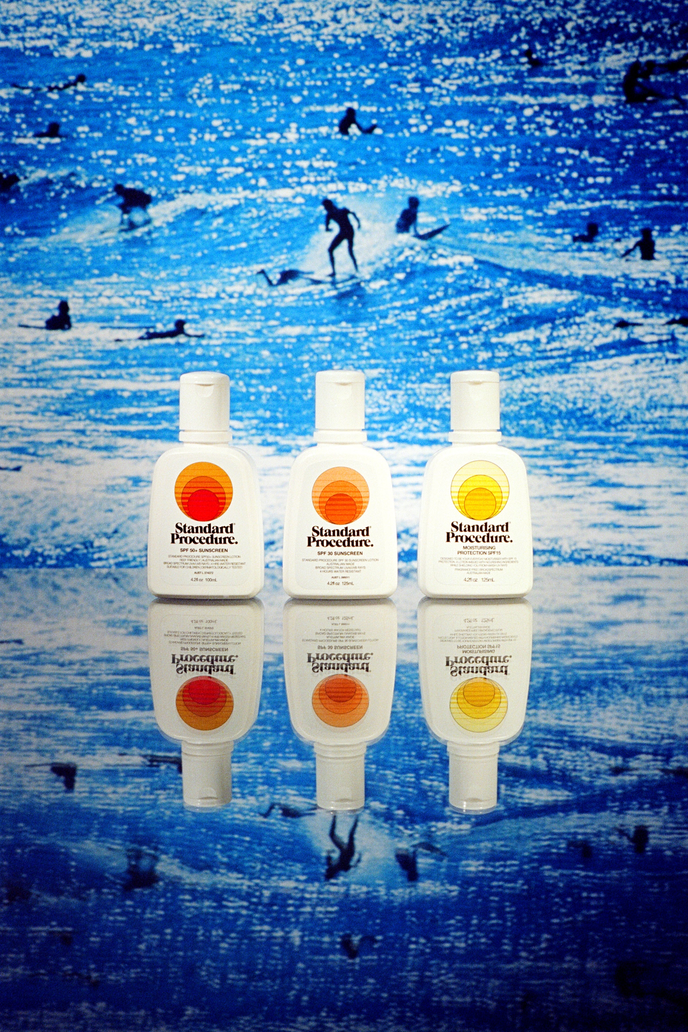 Standard Procedure SPF 50+, SPF 30, and SPF 15 sunscreens lined up against a surf scene.
