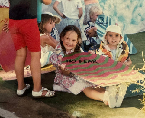 Photo of Sunscreen brand, Standard procedure, founder, Zepha Jackson as a child holding a surf board cut out painted in colours saying No Fear