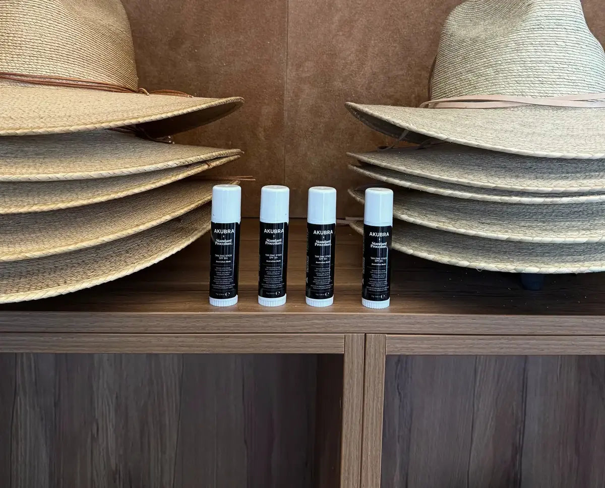 Four Akubra x Standard Procedure Tan Zinc Stick SPF 50+ tubes beside straw hats.