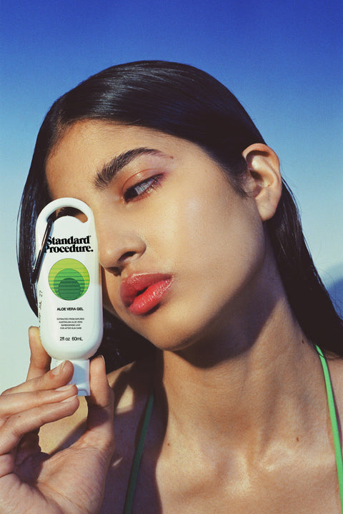 Close-up of a woman holding a Standard Procedure Aloe Vera Gel 60ml tube against a clear blue sky.