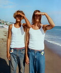 Two people wearing white tank tops and blue jeans on a beach with Sunscreen clipped into their belt buckle