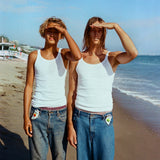 Two people wearing white tank tops and blue jeans on a beach with Sunscreen clipped into their belt buckle
