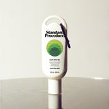 Standard Procedure Aloe Vera Gel 60ml travel tube with a carabiner clip on a reflective surface.