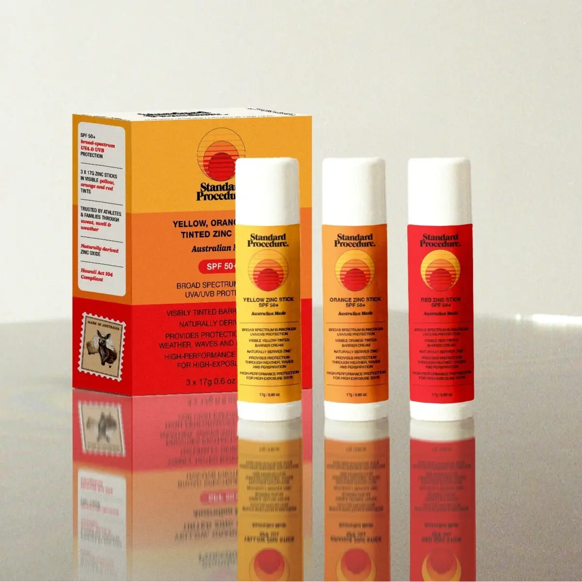 Standard Procedure yellow, orange and red zinc sunscreen sticks SPF 50+ beside retail box.
