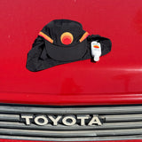 Black surf cap featuring the Standard Procedure logo placed on a red surface beside a small bottle of sunscreen, emphasizing stylish and practical sun protection essentials