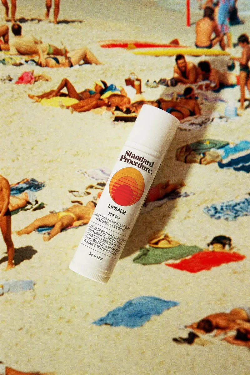 Standard Procedure SPF 50+ lip balm stick against a vintage crowded beach backdrop.