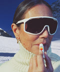 Woman applying Standard Procedure SPF 50 Lip Balm on a snowy mountain wearing white ski goggles and a turtleneck.