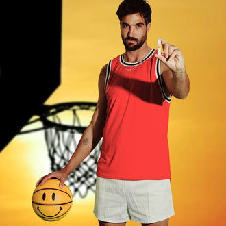Basketball player in red jersey holds up SPF 50 lip balm beside a sunset-lit hoop.