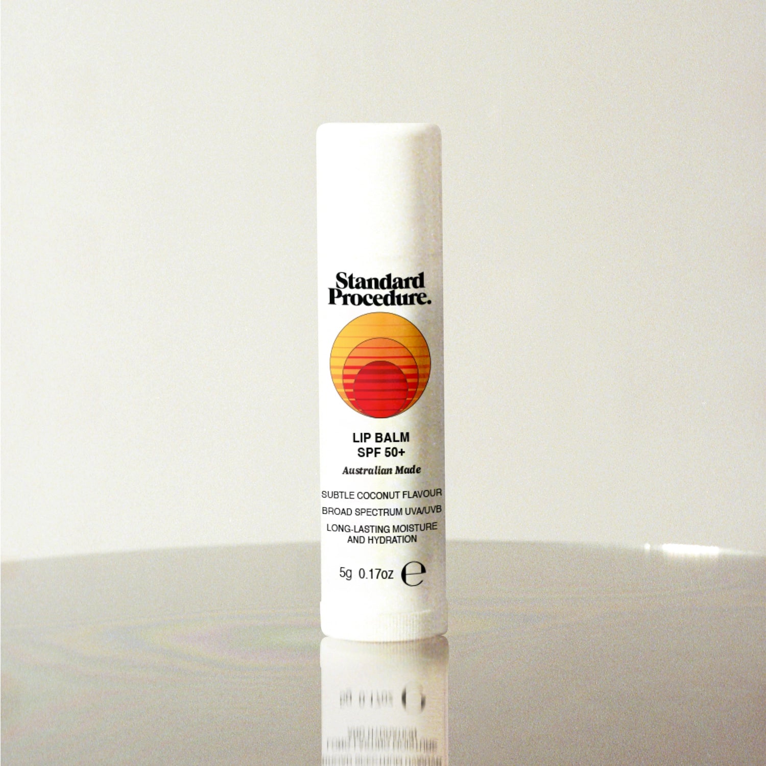 Standard Procedure Lip Balm SPF 50 in coconut flavour with the sunset logo on a reflective surface.