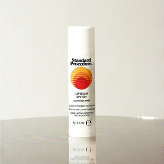 Standard Procedure Lip Balm SPF 50 in coconut flavour with the sunset logo on a reflective surface.