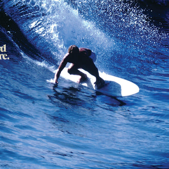 Surfer carving a deep blue wave, branded lifestyle shot for Standard Procedure aloe vera after-sun gel.
