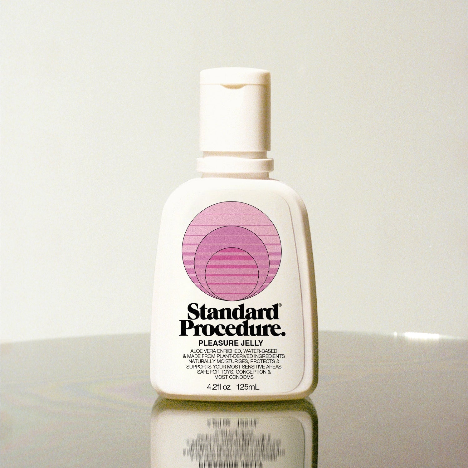 Standard Procedure Pleasure Jelly 125ml bottle with a pump top and pink logo on a reflective surface.