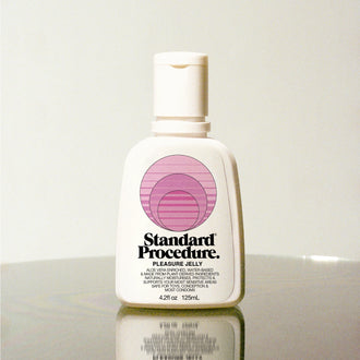 Standard Procedure Pleasure Jelly 125ml bottle with a pump top and pink logo on a reflective surface.