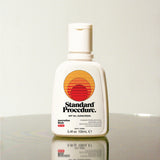 Standard Procedure SPF 50 Sunscreen 100ml bottle with the sunset logo on a reflective surface.