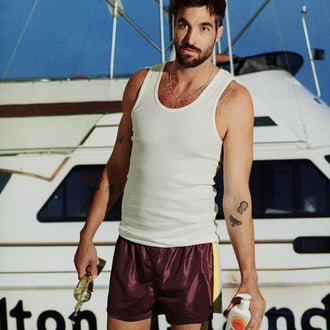 Man holding a Standard Procedure SPF 50 Sunscreen 500ml bottle in front of a fishing boat at a marina.