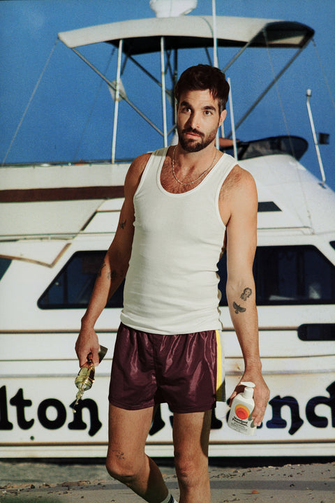 Man holding a Standard Procedure SPF 50 Sunscreen 500ml bottle in front of a fishing boat at a marina.