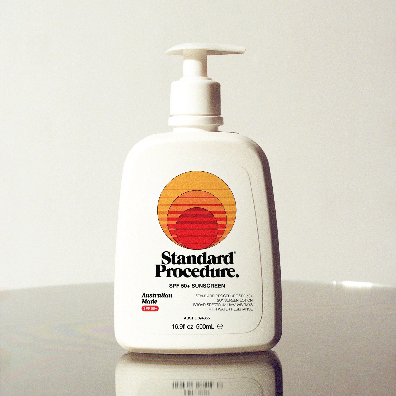Standard Procedure SPF 50 Sunscreen 500ml pump bottle with the sunset logo on a reflective surface.