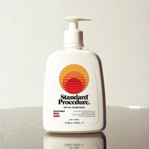 Standard Procedure SPF 50 Sunscreen 500ml pump bottle with the sunset logo on a reflective surface.