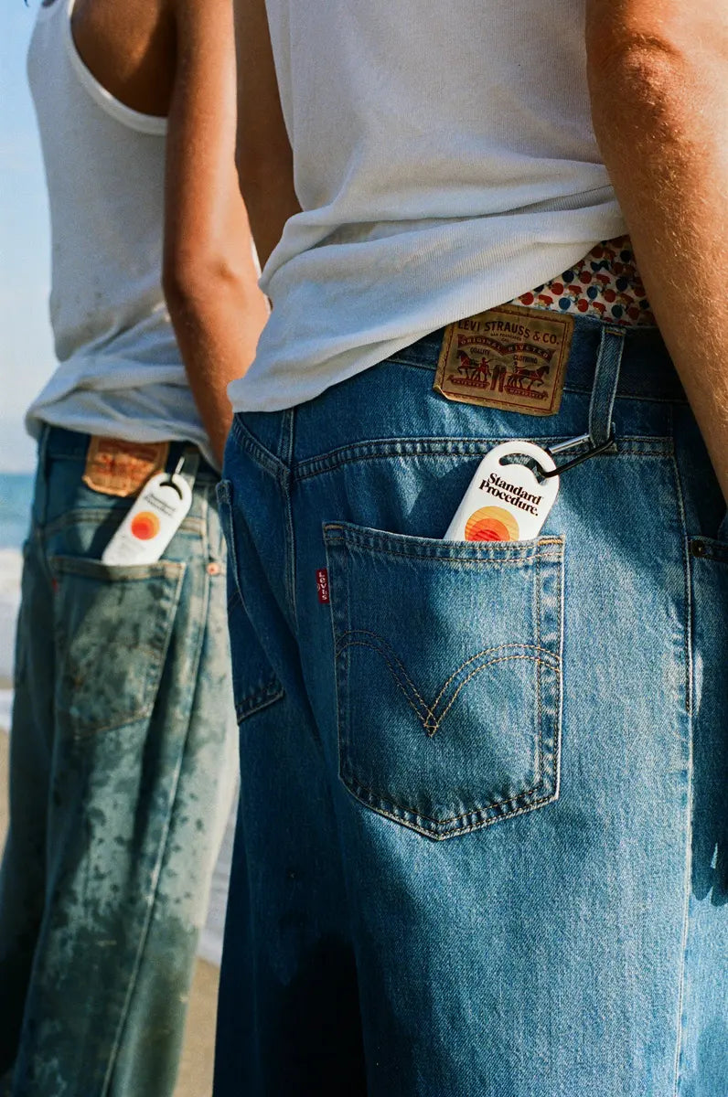 Pocket sized sunscreen from Standard Procedure tucked into denim jeans pockets, showing its compact, travel-friendly design ideal for easy beachside sun protection