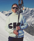 Person in ski gear with skis and poles against a snowy mountain backdrop