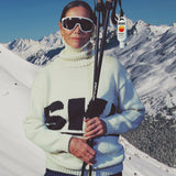 Person in ski gear with skis and poles against a snowy mountain backdrop