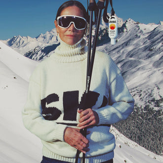 Person in ski gear with skis and poles against a snowy mountain backdrop