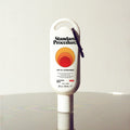 Standard Procedure SPF 50 Sunscreen 60ml travel tube with a carabiner clip on a reflective surface.