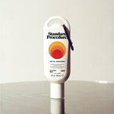 Standard Procedure SPF 50 Sunscreen 60ml travel tube with a carabiner clip on a reflective surface.